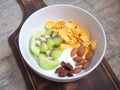 Greek yogurt in a white bowl topped with kiwi, almonds, dried strawberries, and cornflakes, on a wooden cutting board