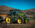 Green agricultural tractor with yellow wheels is slowly driving through a lush green field