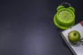 Green alarm clock with green apple on top of the bunch of books