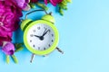 Green alarm clock with spring flowers and space for text on blue background, flat lay. Time change Royalty Free Stock Photo