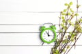 Green alarm clock and young birch branches with first leaves and buds on a white wooden background Royalty Free Stock Photo