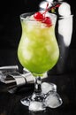 Green alcoholic ocktail with maraschino cherries in hurricane glass, dark bar counter background, selective focus Royalty Free Stock Photo