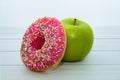 Green apple and donut with strawberry icing and multicolored sprinkles on light wooden table Royalty Free Stock Photo