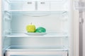 Green apple with measuring tape on white plate in open empty refrigerator