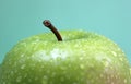 Green apple with numerous water drops on a blue background