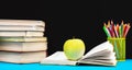 Green apple on opened book with stack of books and colored pencils against chalkboard. Back to school Royalty Free Stock Photo