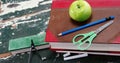 A green apple sits atop a stack of books next to a blue pencil, compass, and scissors Royalty Free Stock Photo