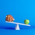 Green apple sitting on seesaw with pork leg on opposite end on blue background