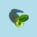 Green apple on stem with leaf on light blue background in bright sunlight with drop shadow. Conceptual minimalist style creative