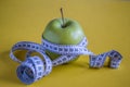 Green apple with white measuring tape on yellow background. Healthy lifestyle concept Royalty Free Stock Photo