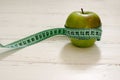 Green apple wrapped in centimeter on white wooden background wit