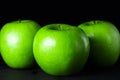 Green apples on a black background. Three apples stand next to each other.