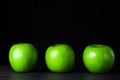 Green apples on a black background. Three apples stand in a row,