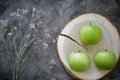 Green apples on a cut of a tree next to a flower on a table