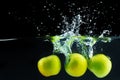 Green apples falling into the water with a splash against black background