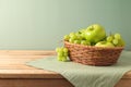 Green apples and grapes in basket on wooden table with tablecloth. Kitchen background