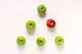 Green apples and one red one are arranged in a pyramid or triangle on a white table. Conceptuality