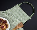Green apron, wooden spatula and plate with pancakes on a dark background