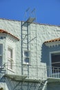 Green aqua colored building with metal fire escape ladder and balcony with red adobe roof tiles and clear blue sky Royalty Free Stock Photo