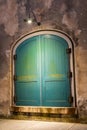 The green arched doors of a warehouse at night with a lone light