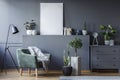 Green armchair between black lamp and plants in grey flat interior with mockup of poster. Real photo Royalty Free Stock Photo