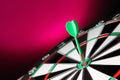 Green arrow hitting target on dart board  magenta background. Space for text Royalty Free Stock Photo