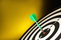 Green arrow hitting target on dart board against yellow background. Space for Royalty Free Stock Photo