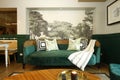 Green Asian sofa with throw pillows and cloth draped over, with wall art of trees at the back