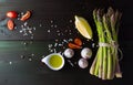 Green asparagus with garlic, salt, lemon, cherry tomato, olive oil and pepper mix on dark background, top view Royalty Free Stock Photo
