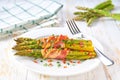 Baked bundles of green asparagus wrapped in bacon in a ceramic plate on a white wooden table Royalty Free Stock Photo