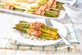 green asparagus wrapped in a roasted slices of bacon in a ceramic plate on a white wooden table Royalty Free Stock Photo