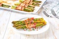 Traditional appetizer, baked bundles of green asparagus wrapped in bacon in a ceramic plate on a white wooden table, close up Royalty Free Stock Photo