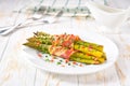 green asparagus wrapped in a roasted slices of bacon in a ceramic plate on a white wooden table, close up Royalty Free Stock Photo