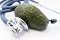 Green avocado raw fruit lies surrounded by stethoscope, which analyse it. Facts and benefits of avocados as tasty, nutritious and