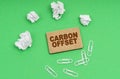 On a green background, crumpled paper, paper clips and a sign with the inscription -Carbon offset