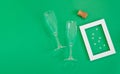 Green background with crystal champagne glasses, cork and white frame with confetti Royalty Free Stock Photo