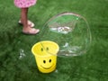 On a green background the girl plays with gromadnymy soap bubbles, yellow bucket with soap foam. Royalty Free Stock Photo