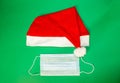 On a green background, a medical mask and a Santa Claus hat. Protection during the Christmas holidays Royalty Free Stock Photo