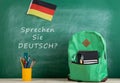 green backpack, blackboard with text "Sprechen Sie Deutsch?", flag of the Germany, school supplies and notebooks Royalty Free Stock Photo