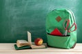 green backpack, open book, red school supplies and apple on the background of the blackboard Royalty Free Stock Photo