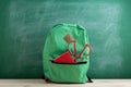 green backpack, red scissors and notebook on the background of the blackboard