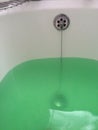 Green bath water in white enamel bath with chrome plug.