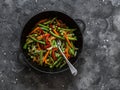 Green beans, sweet peppers, carrots, onions, green peas stir fry in a pan on a dark background, top view. Fast diet vegetarian