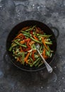 Green beans, sweet peppers, carrots, onions, green peas stir fry in a pan on a dark background, top view. Fast diet vegetarian