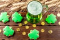 Green beer in a glass mug with gingerbread clover, horseshoe, wheat spike and gold coins on a rustic wooden surface. Festive