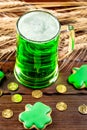 Green beer in a glass mug with gingerbread clover, horseshoe, wheat spike and gold coins on a rustic wooden surface. Festive