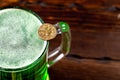 Green beer in a glass mug with gold coins on a rustic wooden surface. Festive background for St. Patrick`s day. Free space