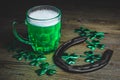 St. Patrick`s Day. Green Beer pint with rusty horseshoe on wooden table, decorated with shamrock leaves.