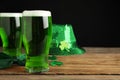Green beer and St Patrick`s Day decor on wooden table against black background. Space for text