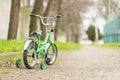 A green bicycle for children with additional wheels at road in park